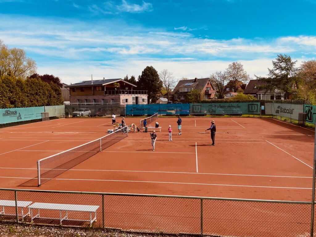 Kinder auf einem Tennisplatz, zusammen mit ihrem Tennistrainer, der sie beim Training anleitet.