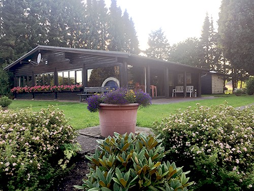 Das braune Holz-Clubhaus der Tennisfreunde Ahrensfelde e.V., eingebettet in die Natur und umgeben von Bäumen.